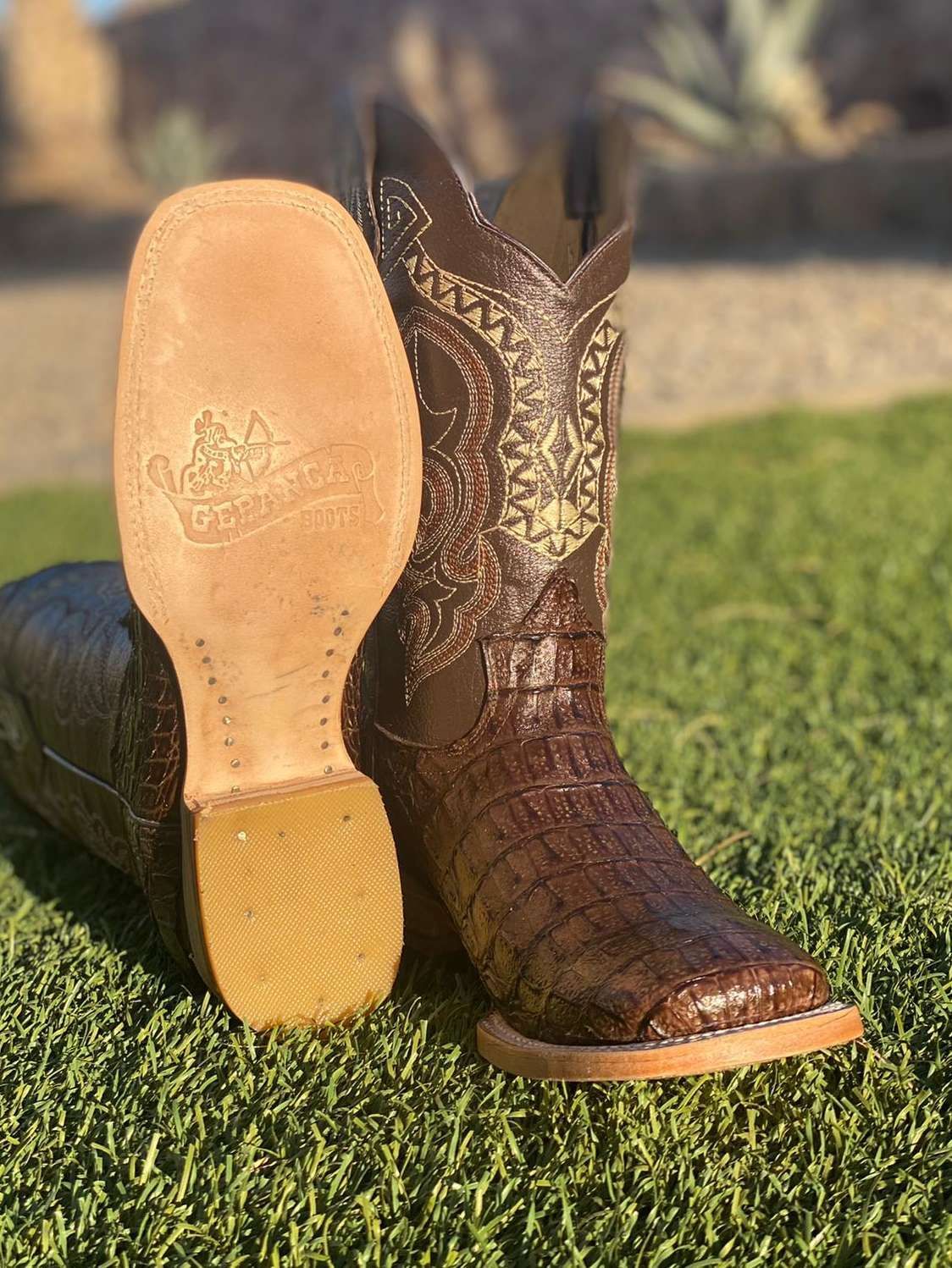 A pair of brown cowboy boots are sitting on top of a lush green field.