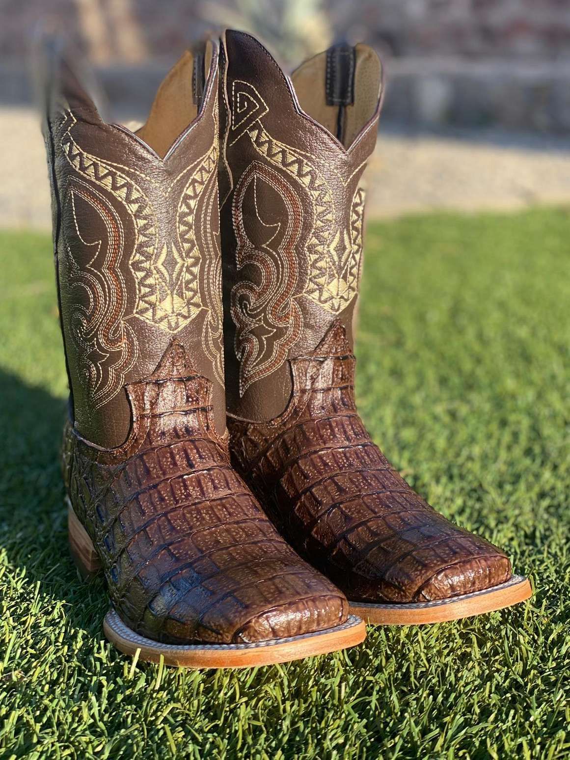 A pair of brown cowboy boots are sitting on top of a lush green field.