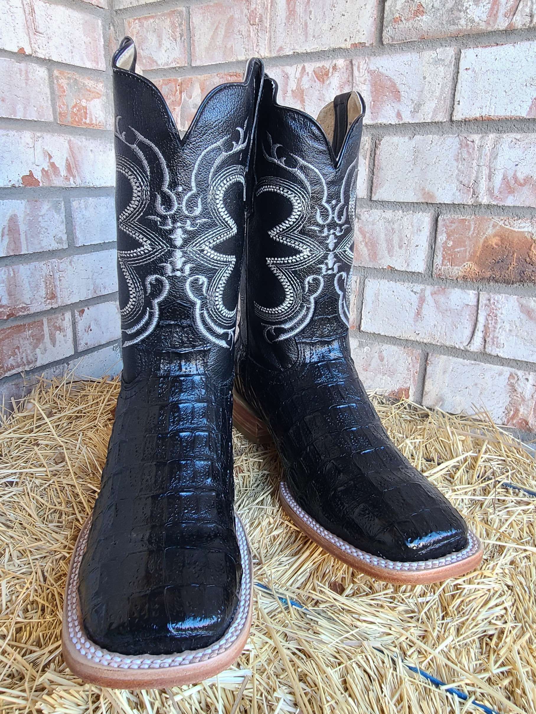 A pair of black cowboy boots are sitting on top of a pile of hay.