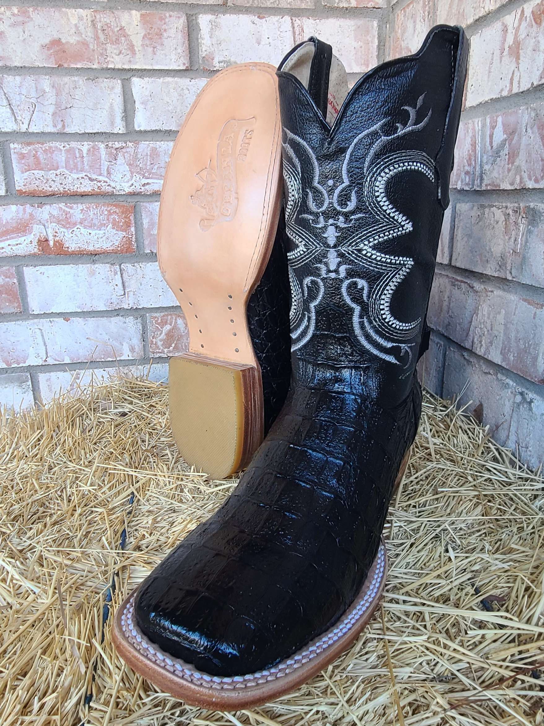 A pair of black cowboy boots are sitting on top of a pile of hay.