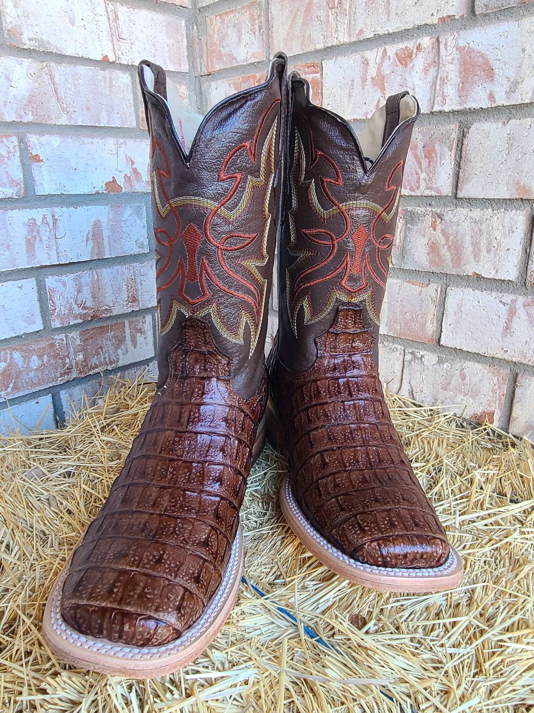 A pair of brown cowboy boots are sitting on top of a pile of hay.