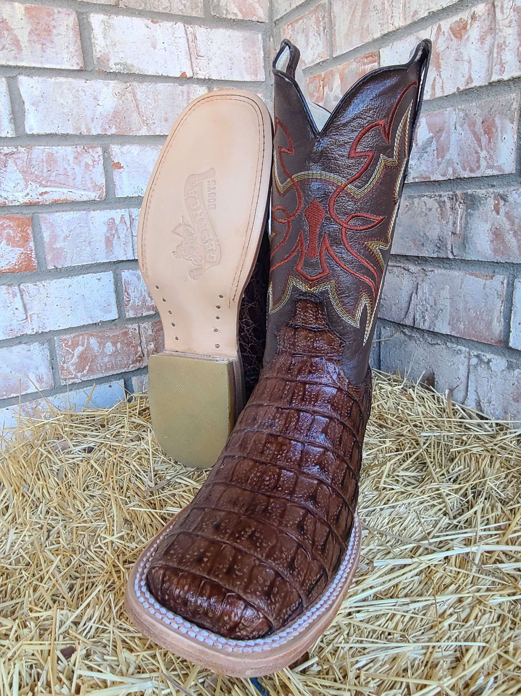A pair of brown cowboy boots are sitting on a pile of hay in front of a brick wall.