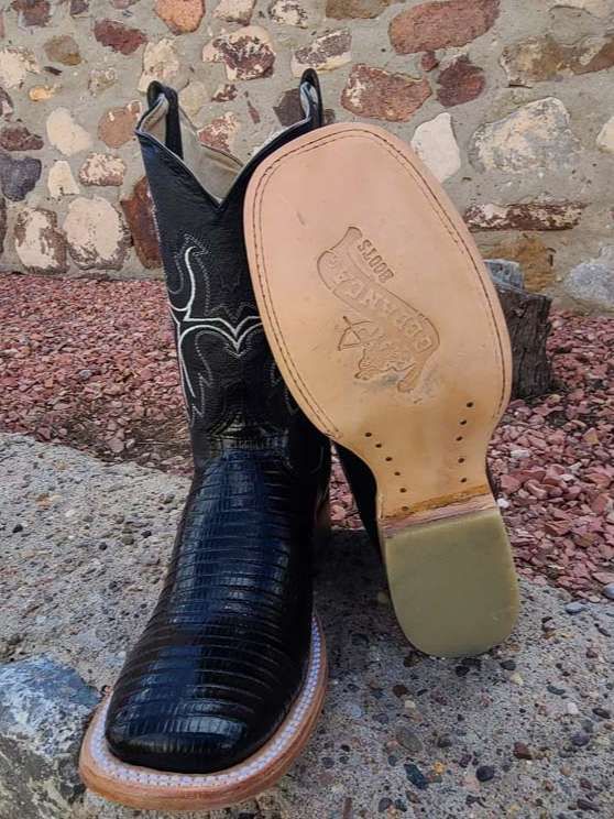 A pair of black cowboy boots are sitting on a rocky surface.