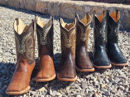 Three pairs of cowboy boots are lined up on gravel.