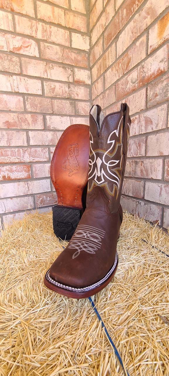 A pair of brown cowboy boots are sitting on top of a pile of hay.