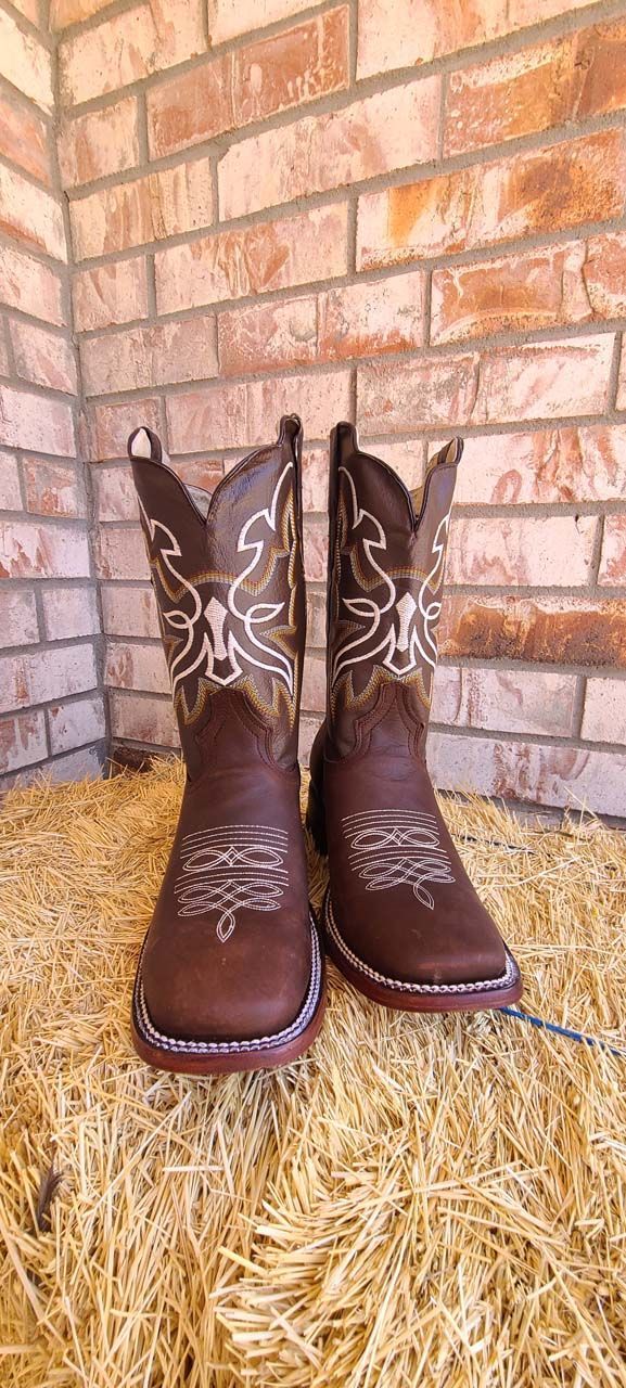 A pair of brown cowboy boots are sitting on top of a pile of hay.