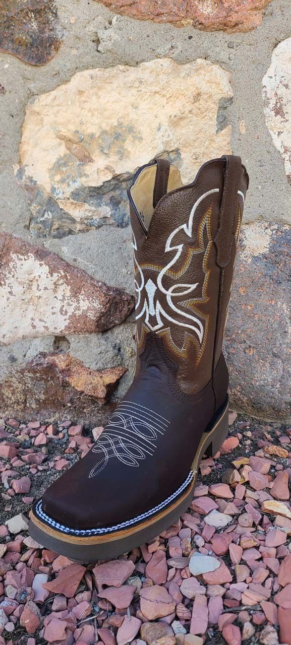 A pair of brown cowboy boots are sitting on a pile of rocks in front of a stone wall.