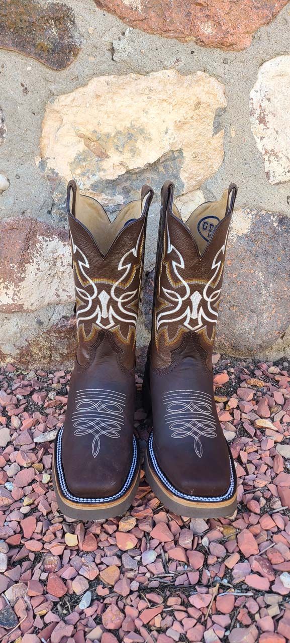 A pair of brown cowboy boots are sitting on a pile of gravel in front of a stone wall.