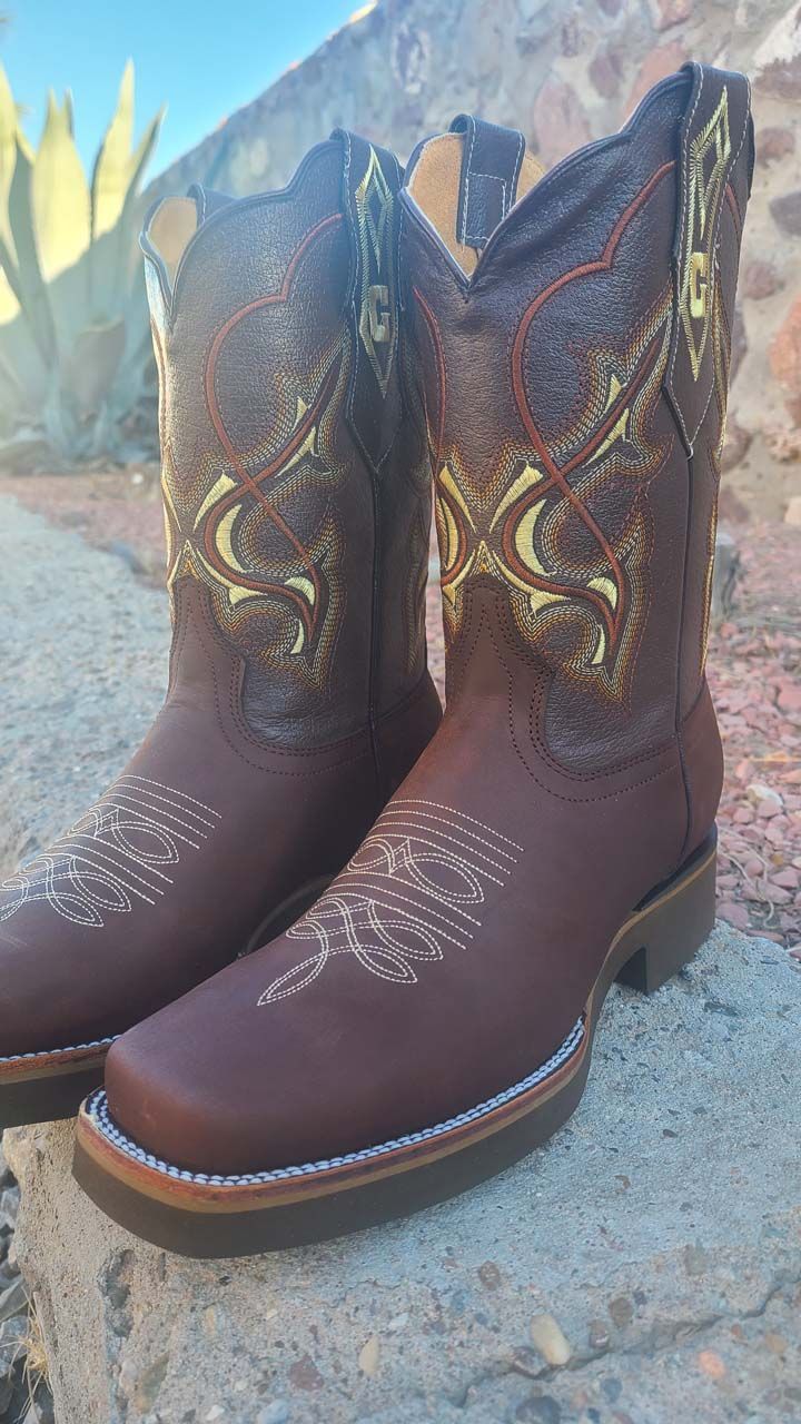 A pair of brown cowboy boots are sitting on a rock.