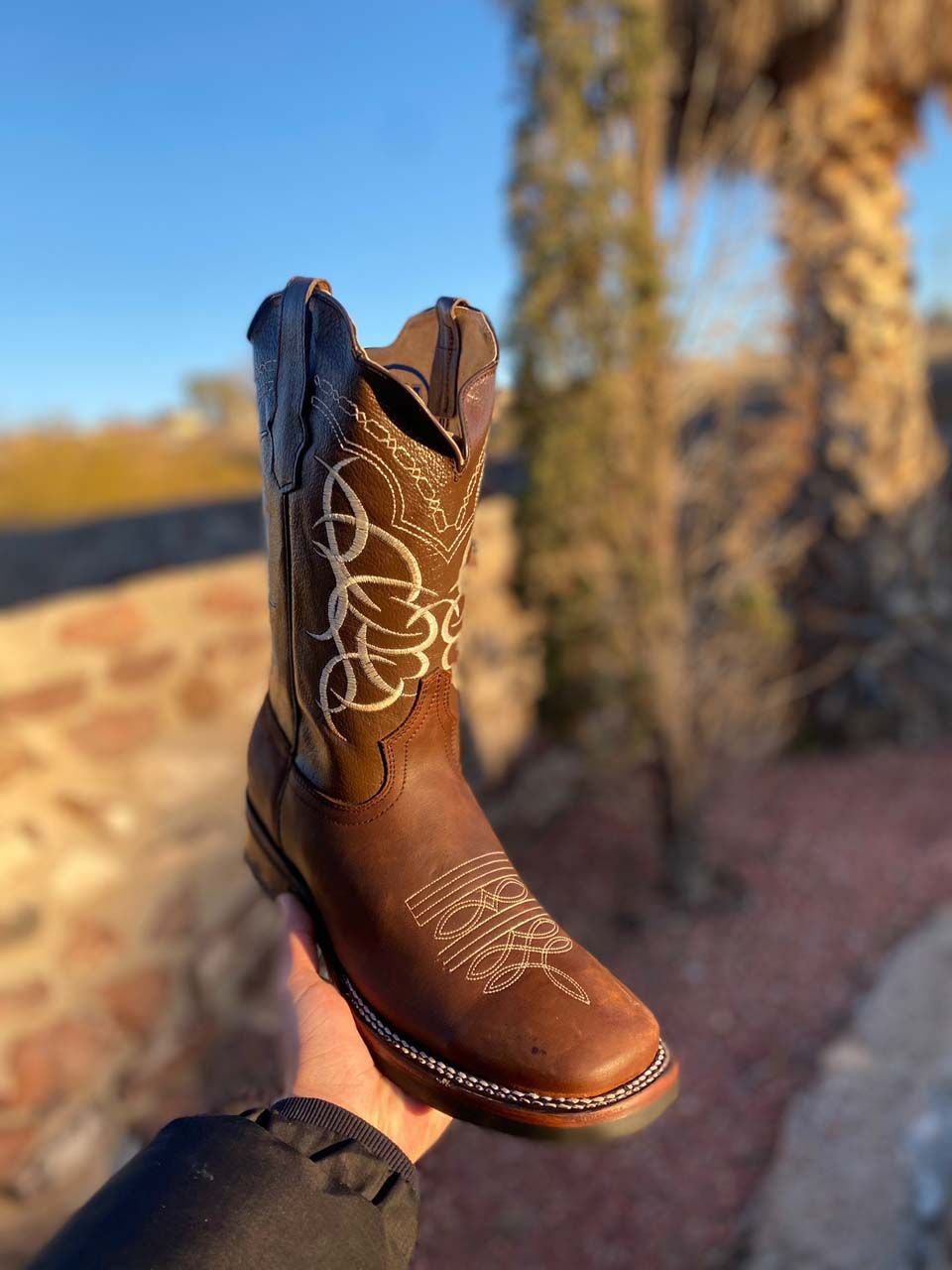 A person is holding a pair of brown cowboy boots in their hand.