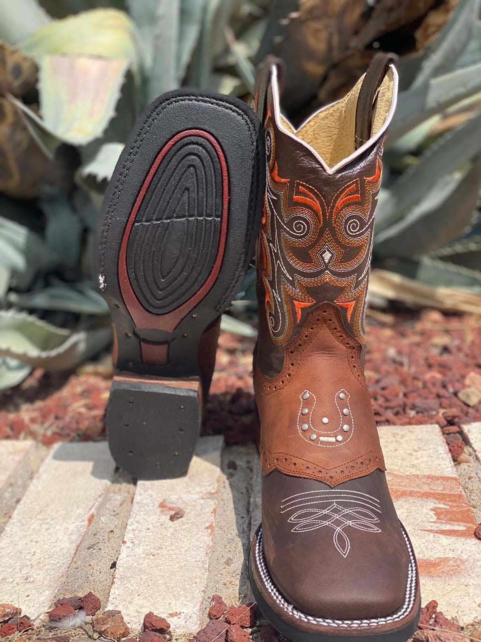 A pair of brown cowboy boots are sitting on top of a pile of rocks.