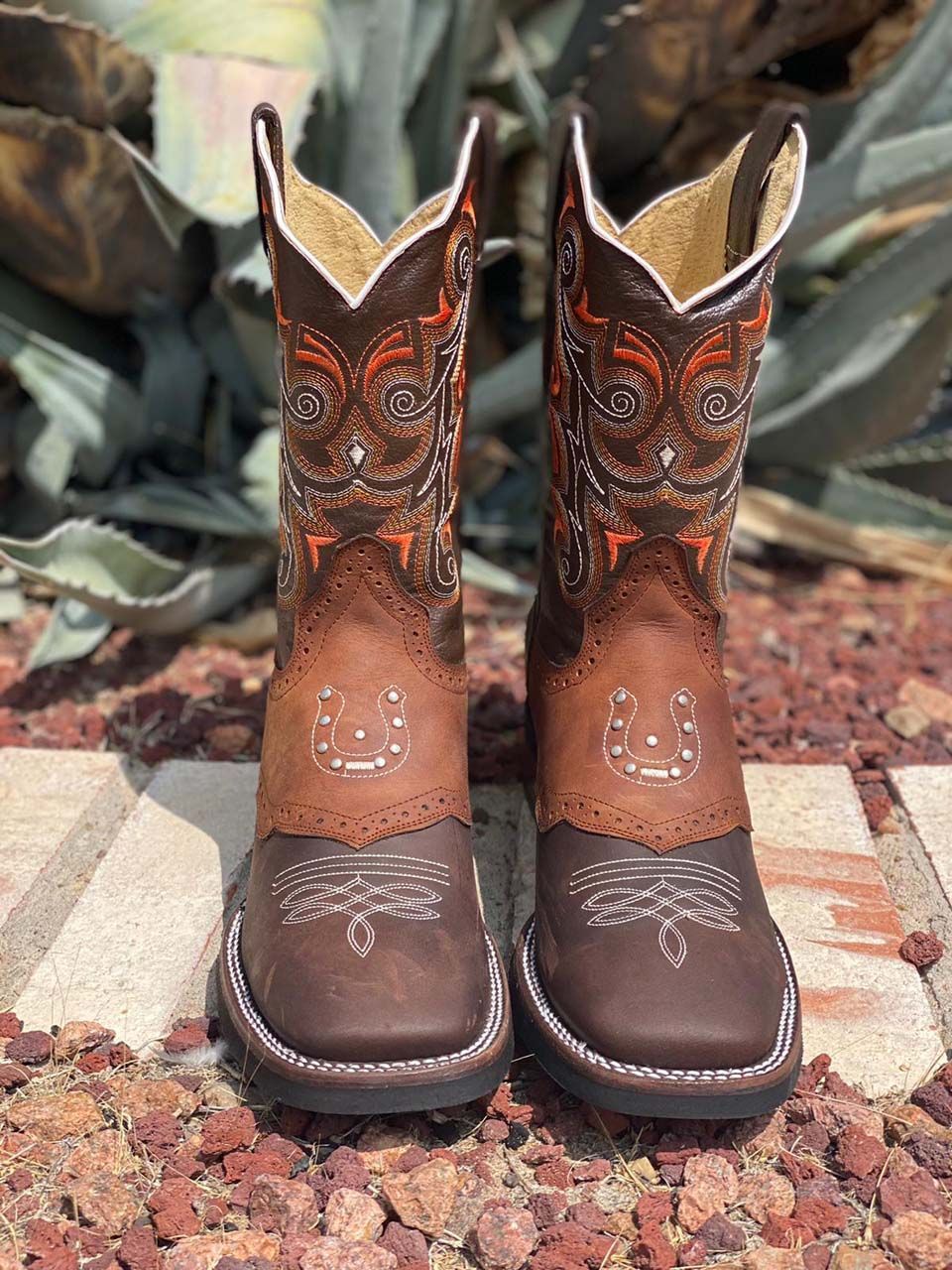 A pair of brown cowboy boots are sitting on top of a pile of rocks.