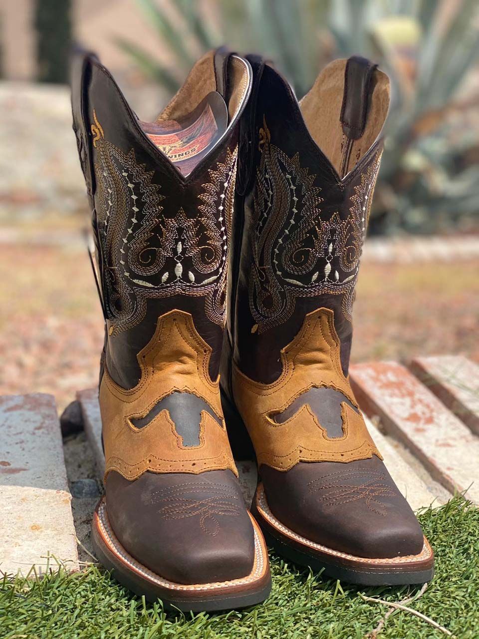 A pair of brown and tan cowboy boots are sitting on top of a wooden table.