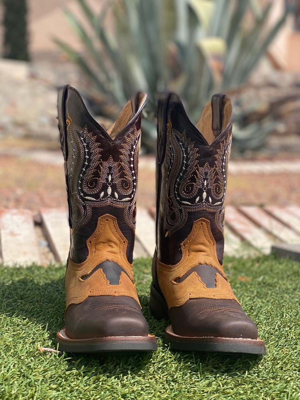 A pair of cowboy boots are sitting on top of a lush green field.