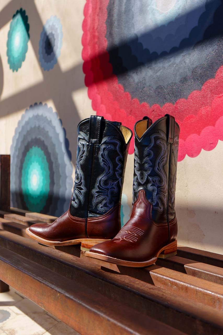 A pair of cowboy boots are sitting on a wooden shelf.