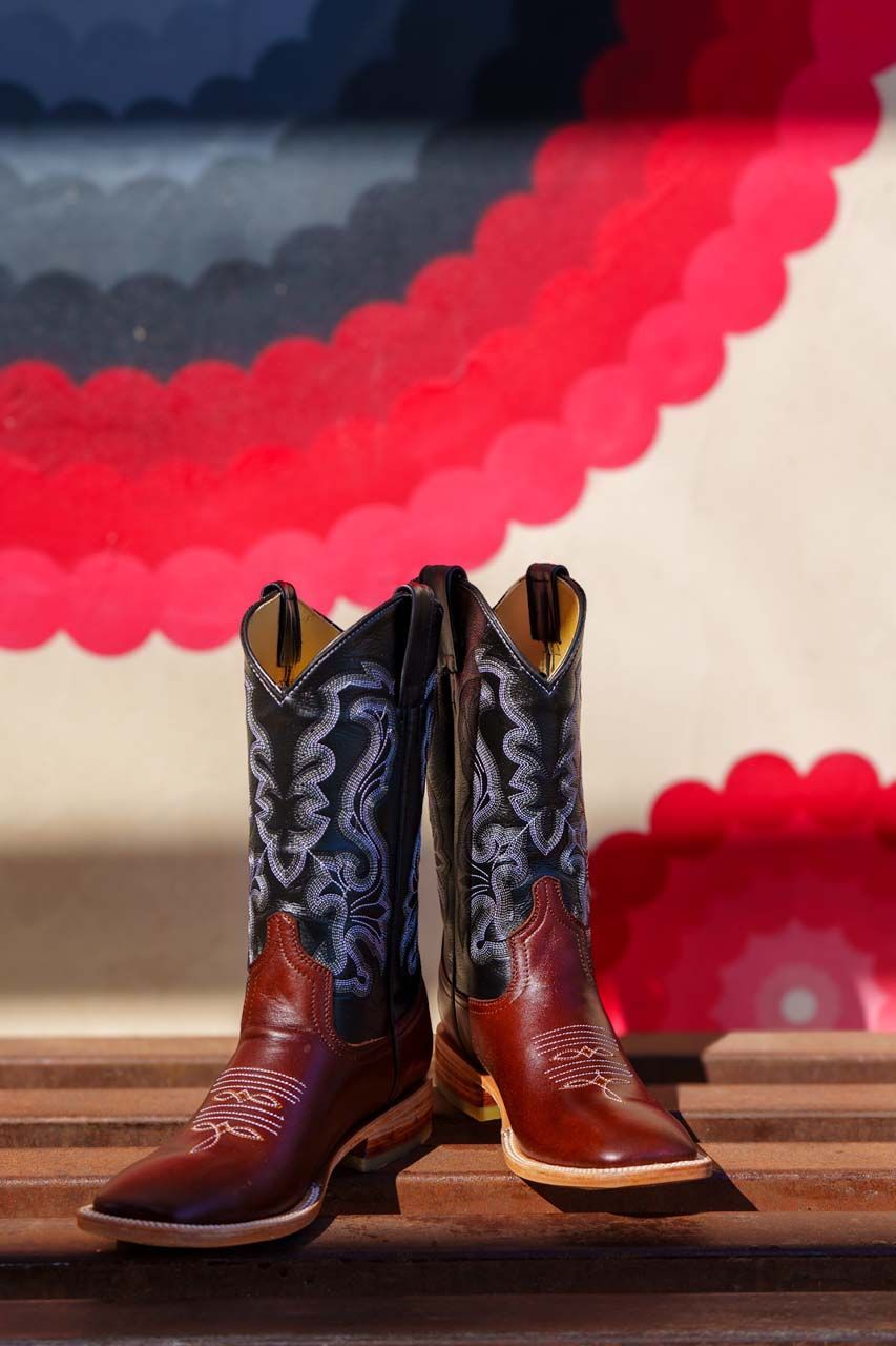 A pair of brown and black cowboy boots are sitting on a wooden bench.