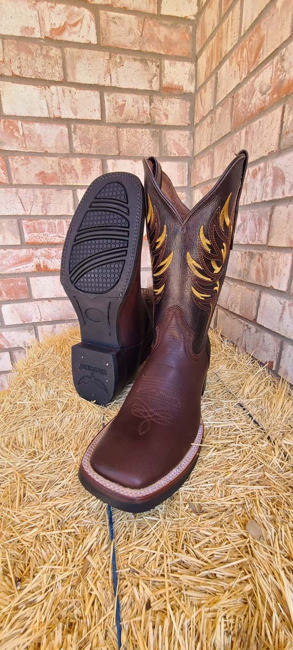 A pair of brown cowboy boots are sitting on top of a pile of hay.