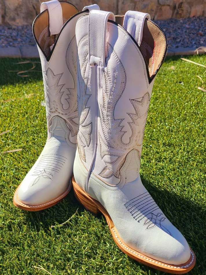 A pair of white cowboy boots are sitting on top of a lush green field.