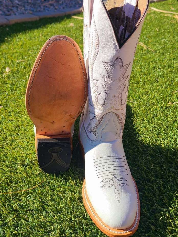 A pair of white cowboy boots are sitting on top of a lush green field.