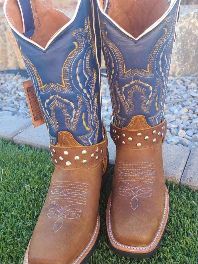 A pair of brown and blue cowboy boots are sitting on the grass.