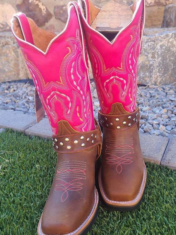 A pair of pink and brown cowboy boots are sitting on top of a lush green field.