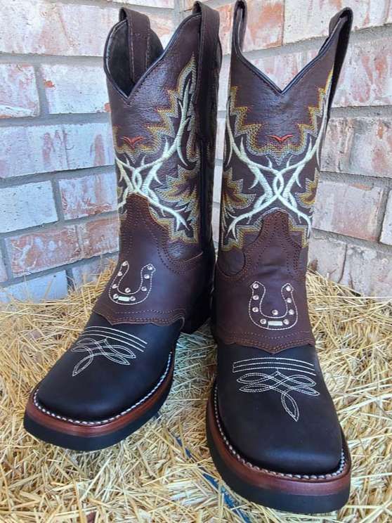 A pair of brown cowboy boots are sitting on a pile of hay.