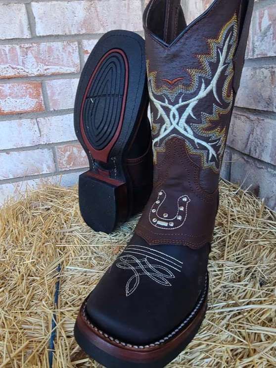 A pair of brown cowboy boots are sitting on a pile of hay.