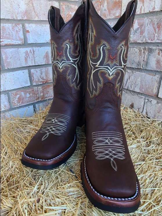 A pair of brown cowboy boots are sitting on a pile of hay.