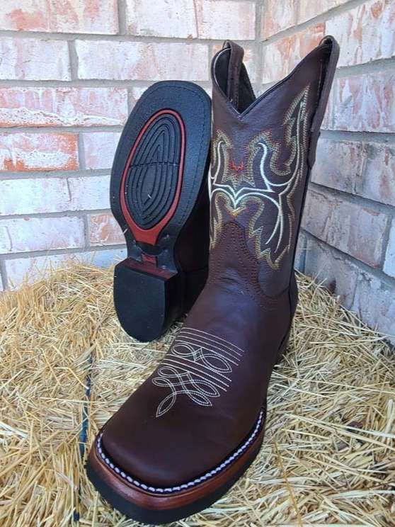 A pair of brown cowboy boots are sitting on top of a pile of hay.