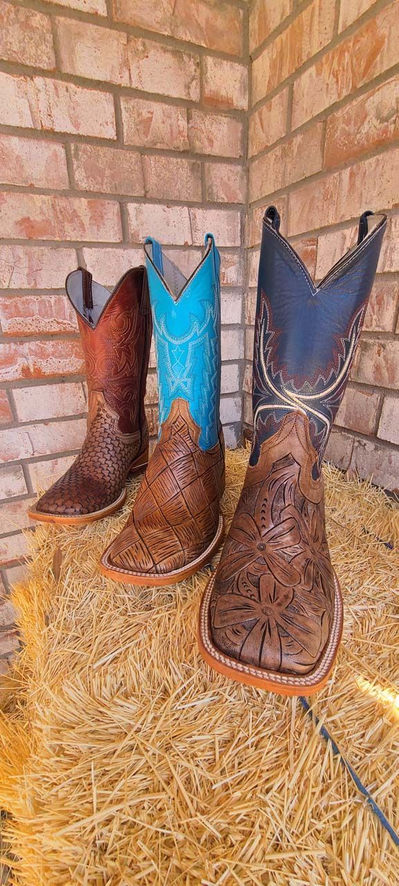 Three pairs of cowboy boots are sitting on top of a pile of hay.
