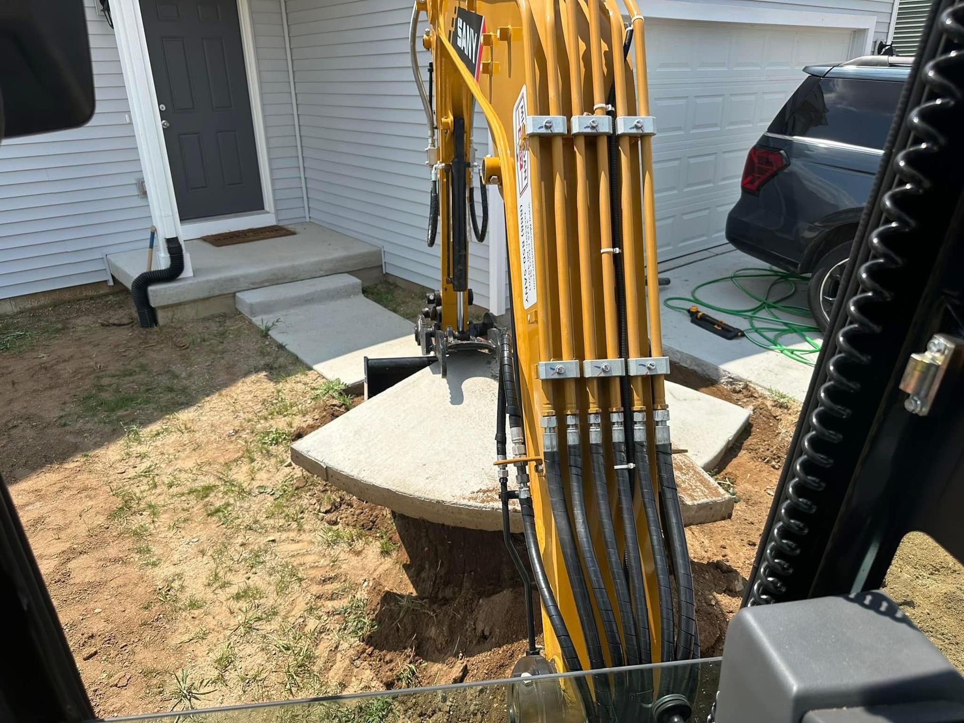 A yellow excavator is digging a hole in the ground in front of a house.