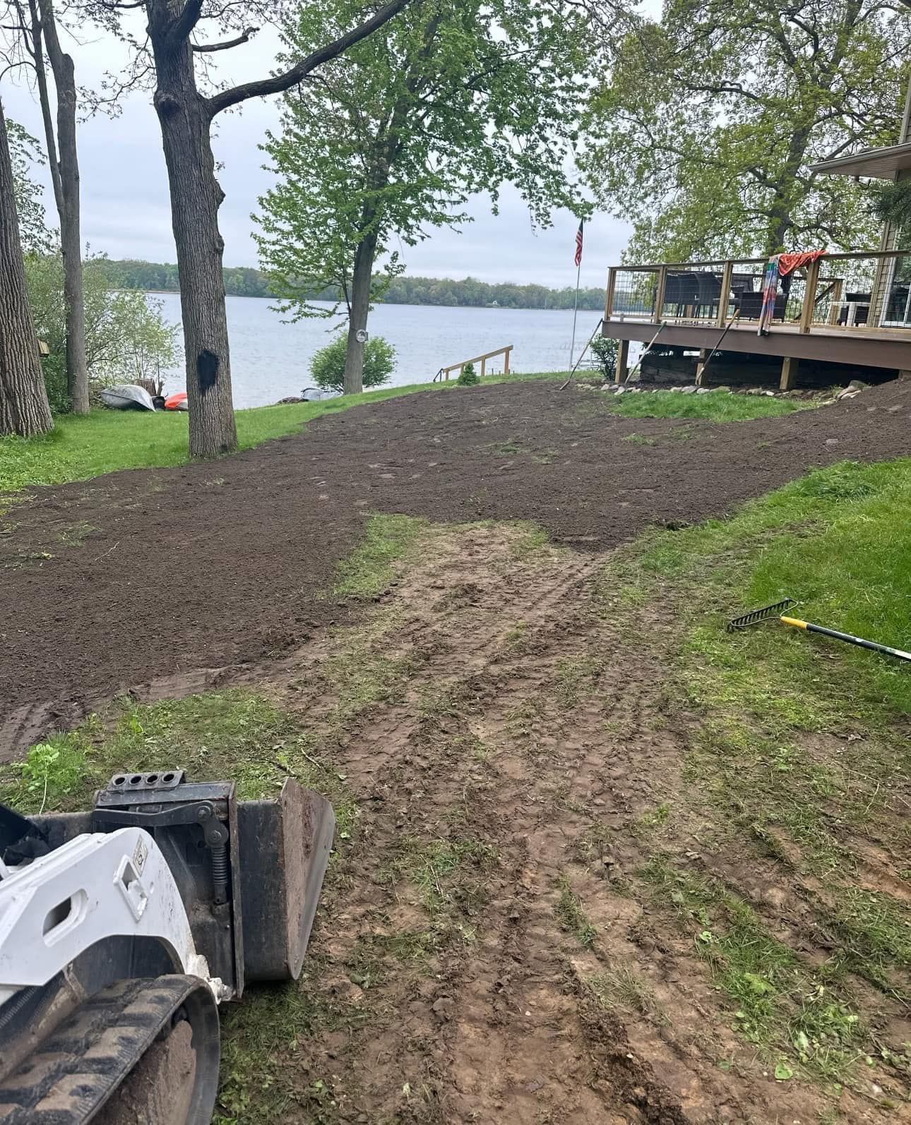 A tractor is driving down a dirt road next to a lake.