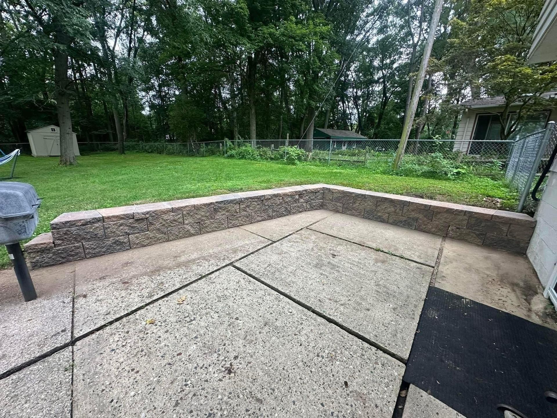 A patio with a grill and trees in the background.