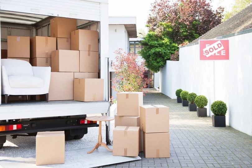 Camion che carica scatole e mobili all'esterno di una casa con un cartello 