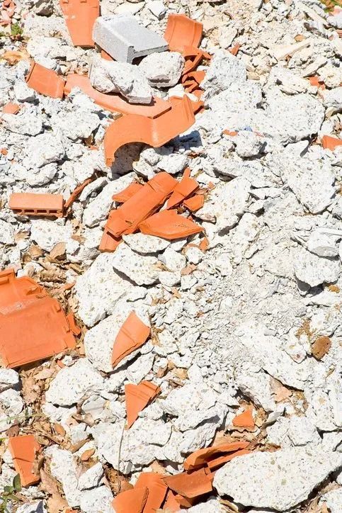 Cumulo di macerie con tegole rosse rotte e detriti di cemento bianco.