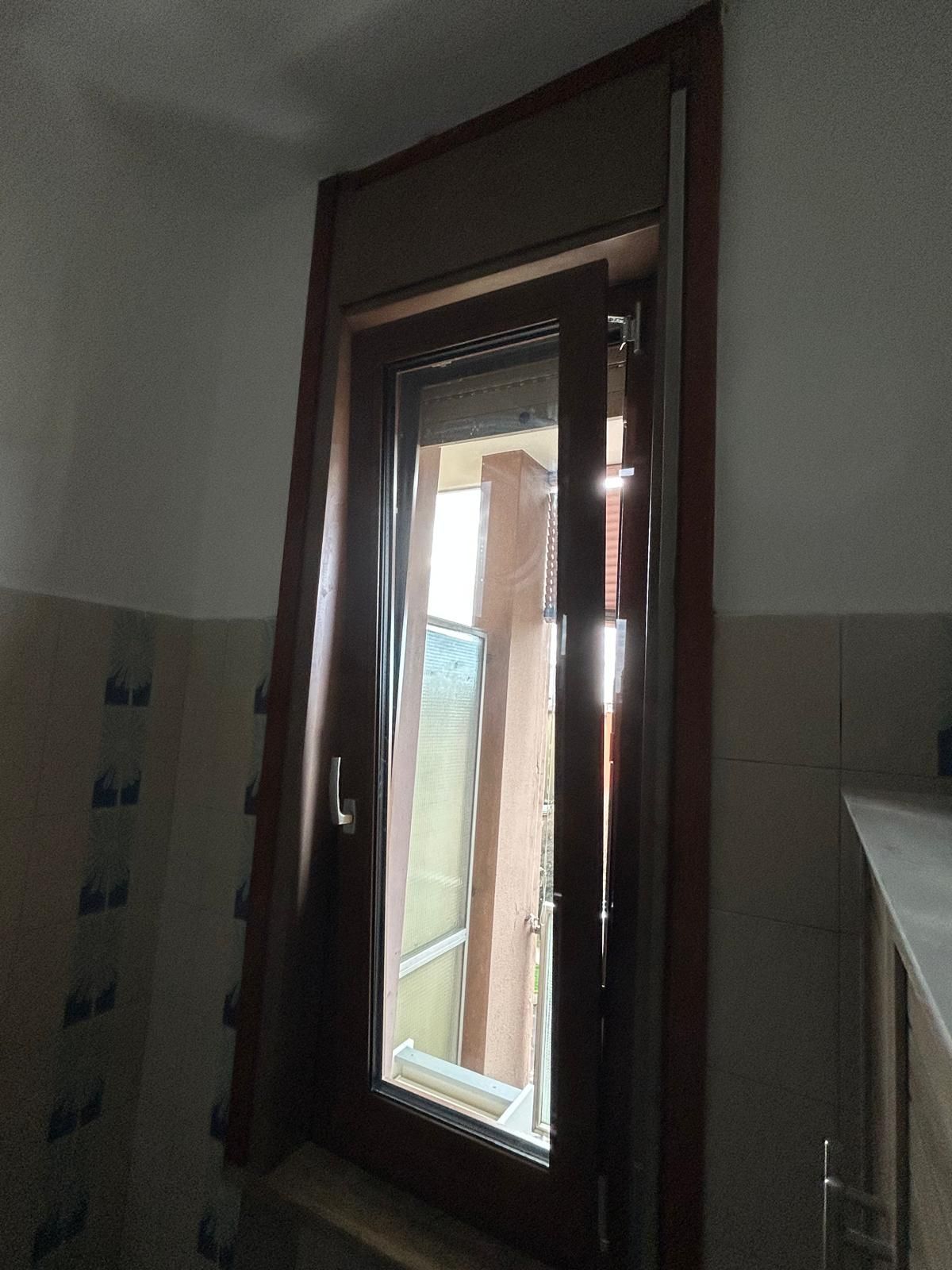 Bagno con WC bianco, piastrelle a motivi, finestra e mobiletto.