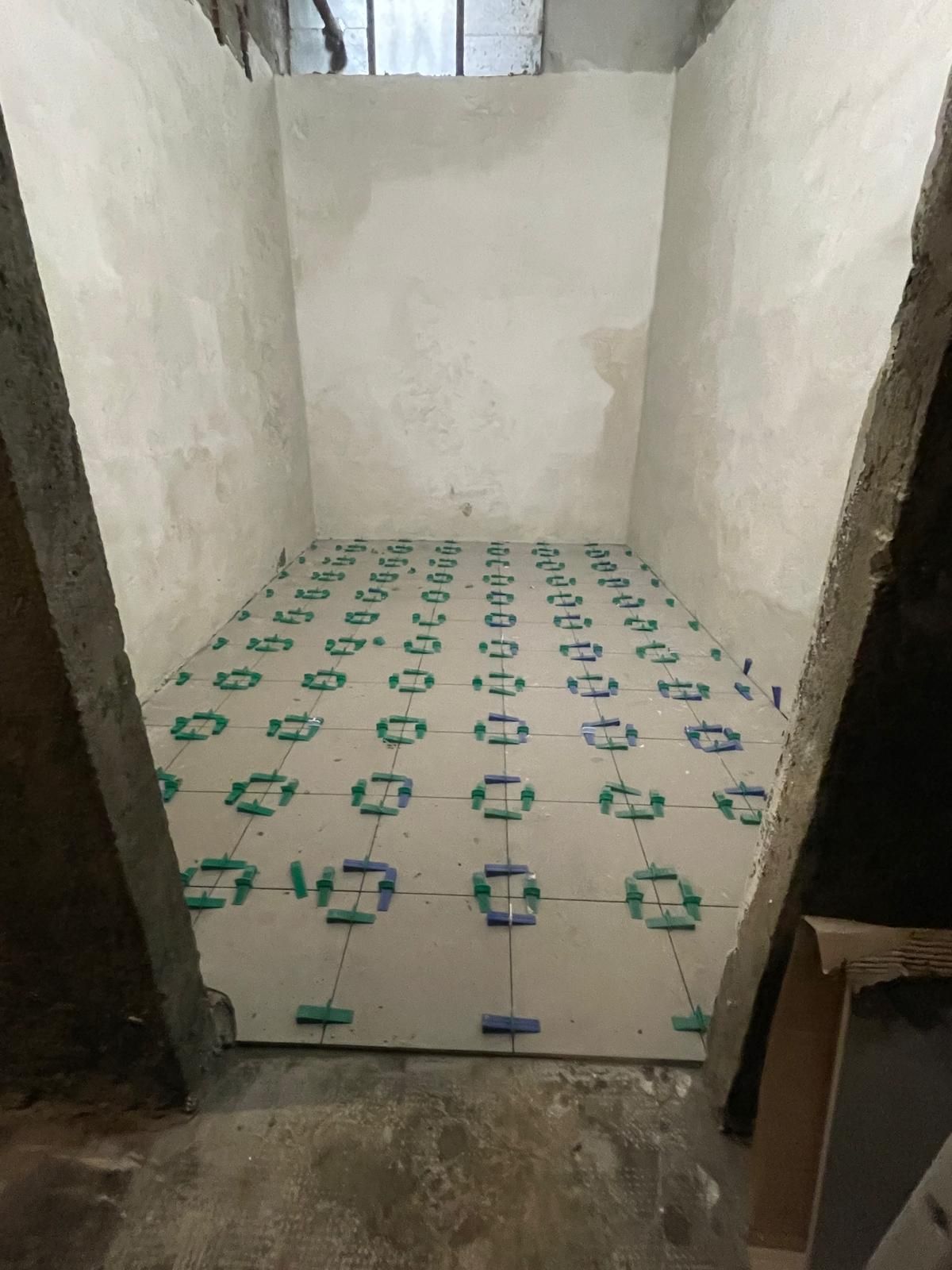 Stanza stretta con pavimento in piastrelle bianche a motivi geometrici. Le pareti sono grigie e bianche, non tinteggiate.