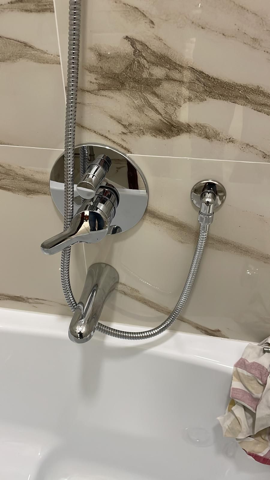 Rubinetto cromato per doccia con doccetta e deviatore in un bagno piastrellato bianco.