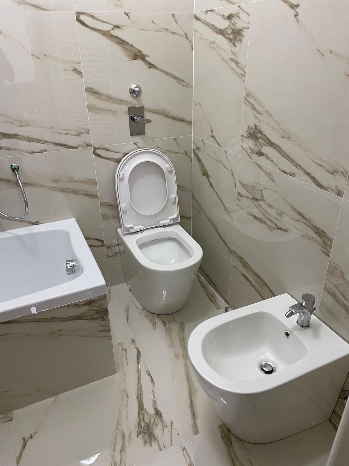 Bagno con WC, bidet e vasca. Pareti e pavimenti sono bianchi con venature marroni.