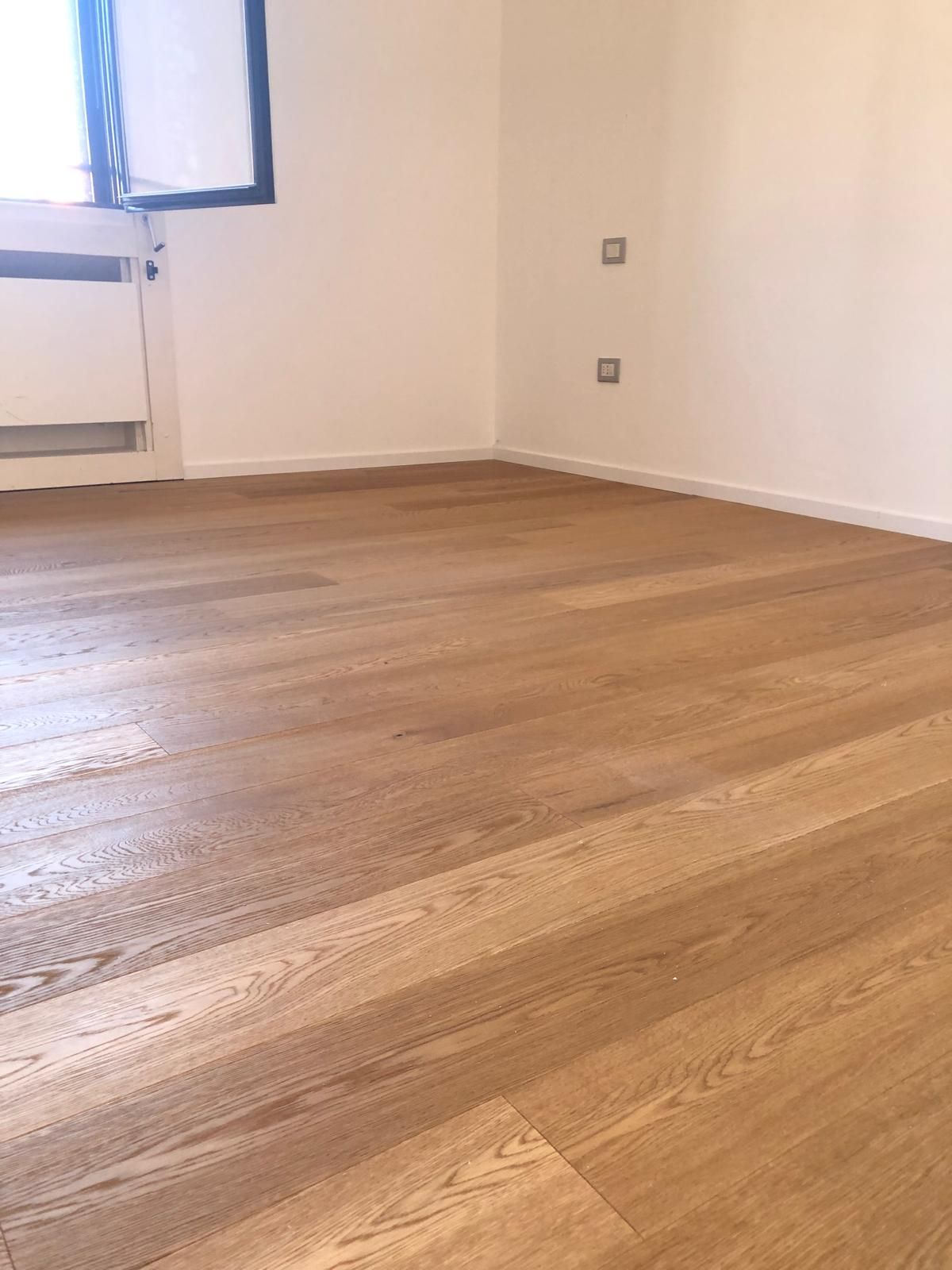 Pavimento in legno massello in una stanza vuota con pareti bianche e una finestra.