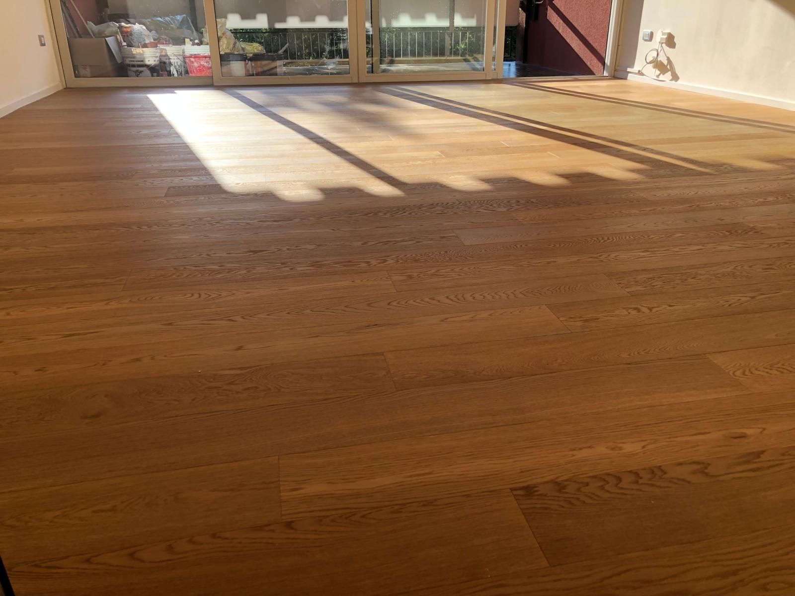 Pavimento in legno in una stanza soleggiata, con ombre visibili provenienti dal telaio di una finestra.