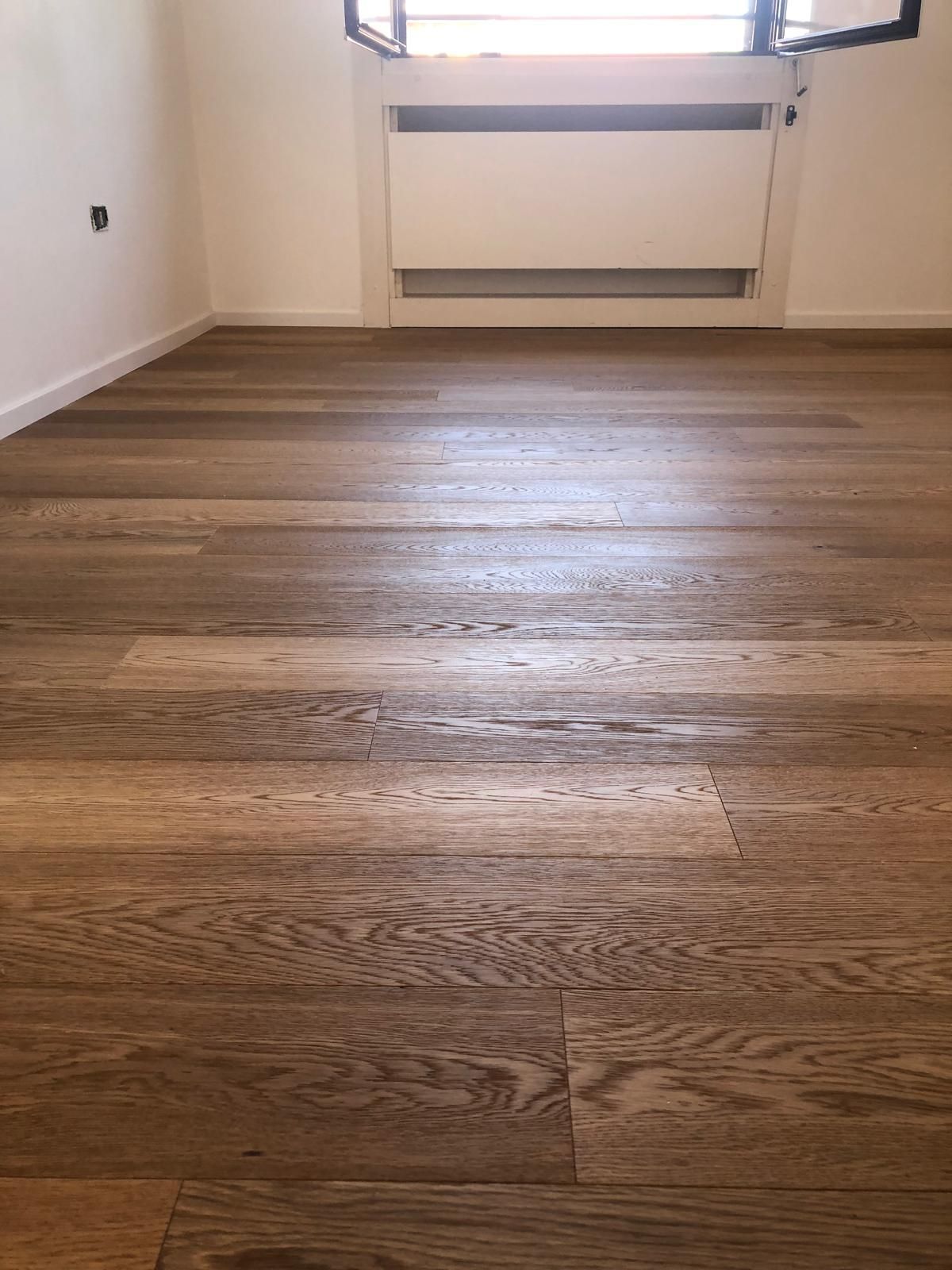 Pavimento in legno in una stanza con parete bianca e termosifone sotto una finestra.