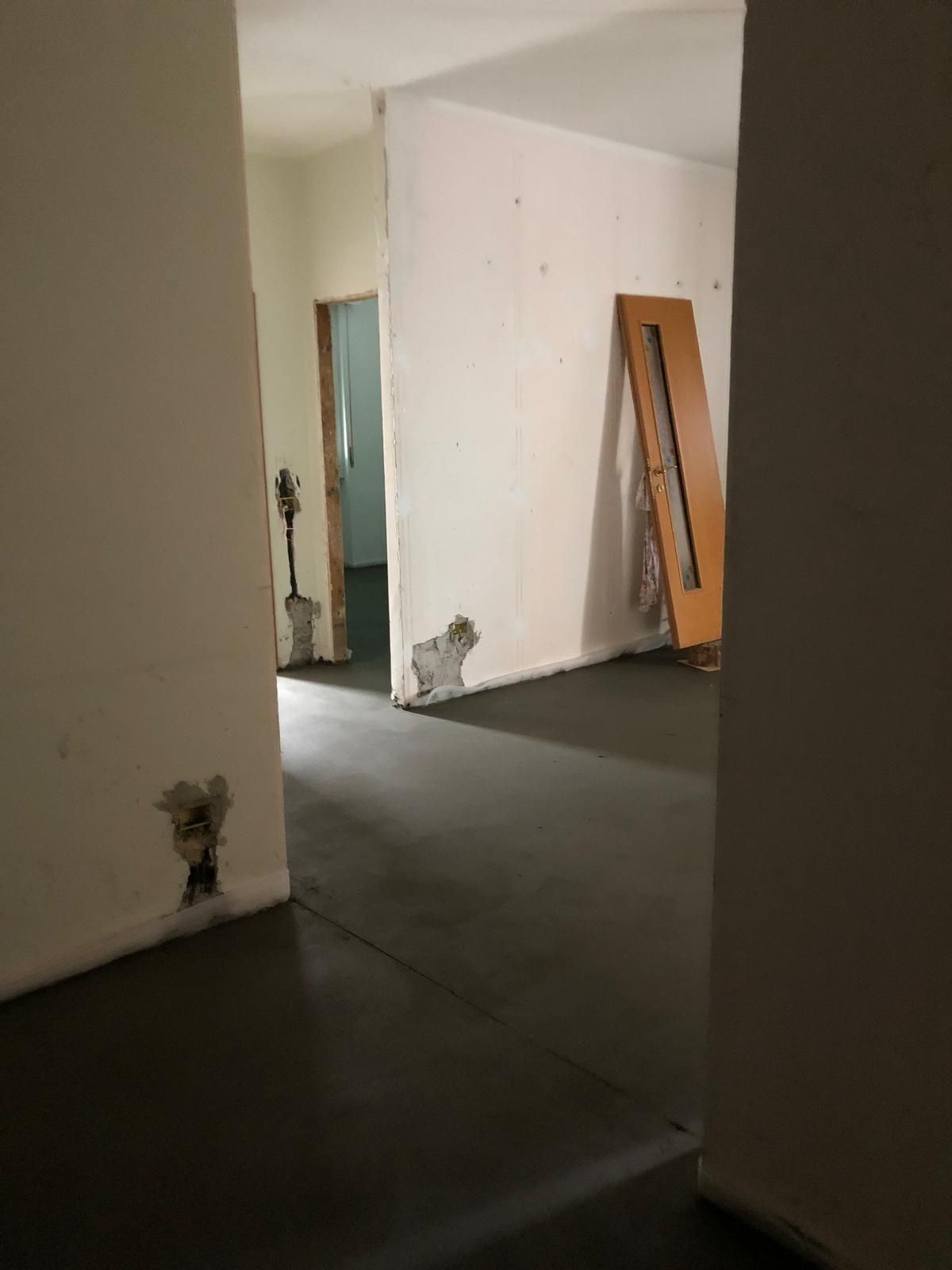 Corridoio con pareti danneggiate e una porta inclinata. Pavimento scuro, pareti bianco sporco.