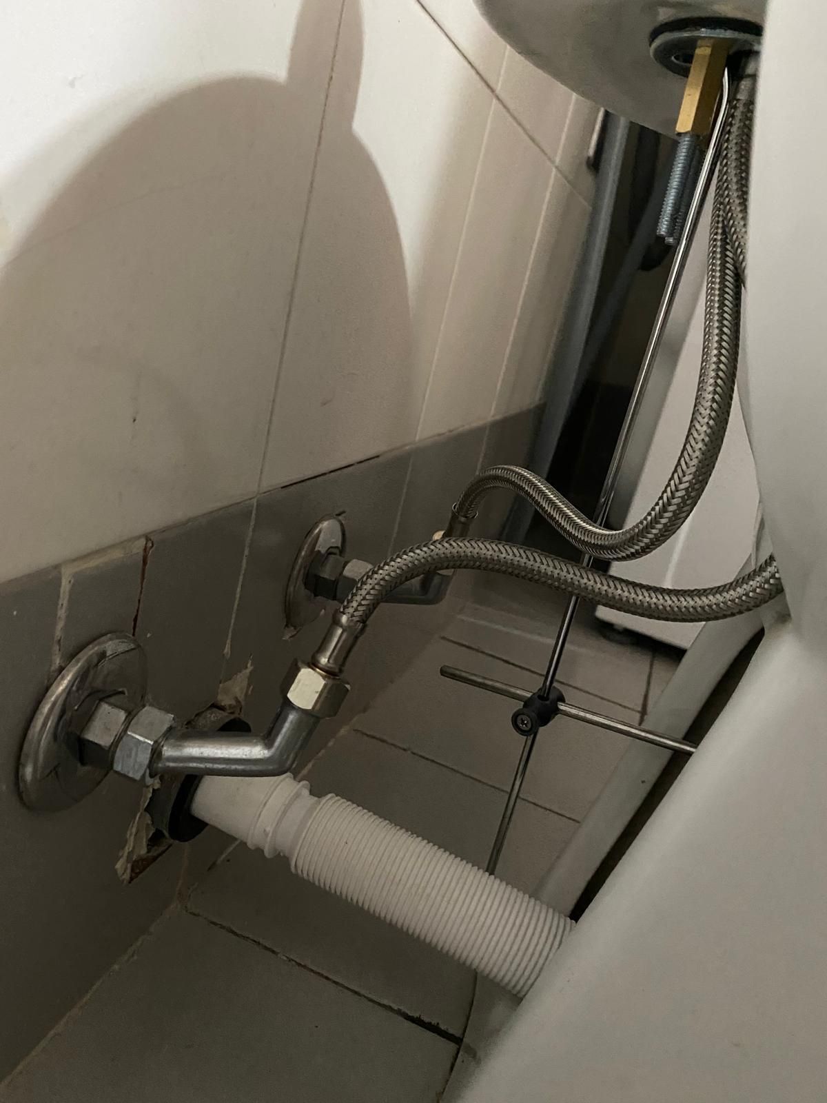 Impianto idraulico sotto il water: tubi di alimentazione dell'acqua e tubo di scarico visibili contro una parete piastrellata.