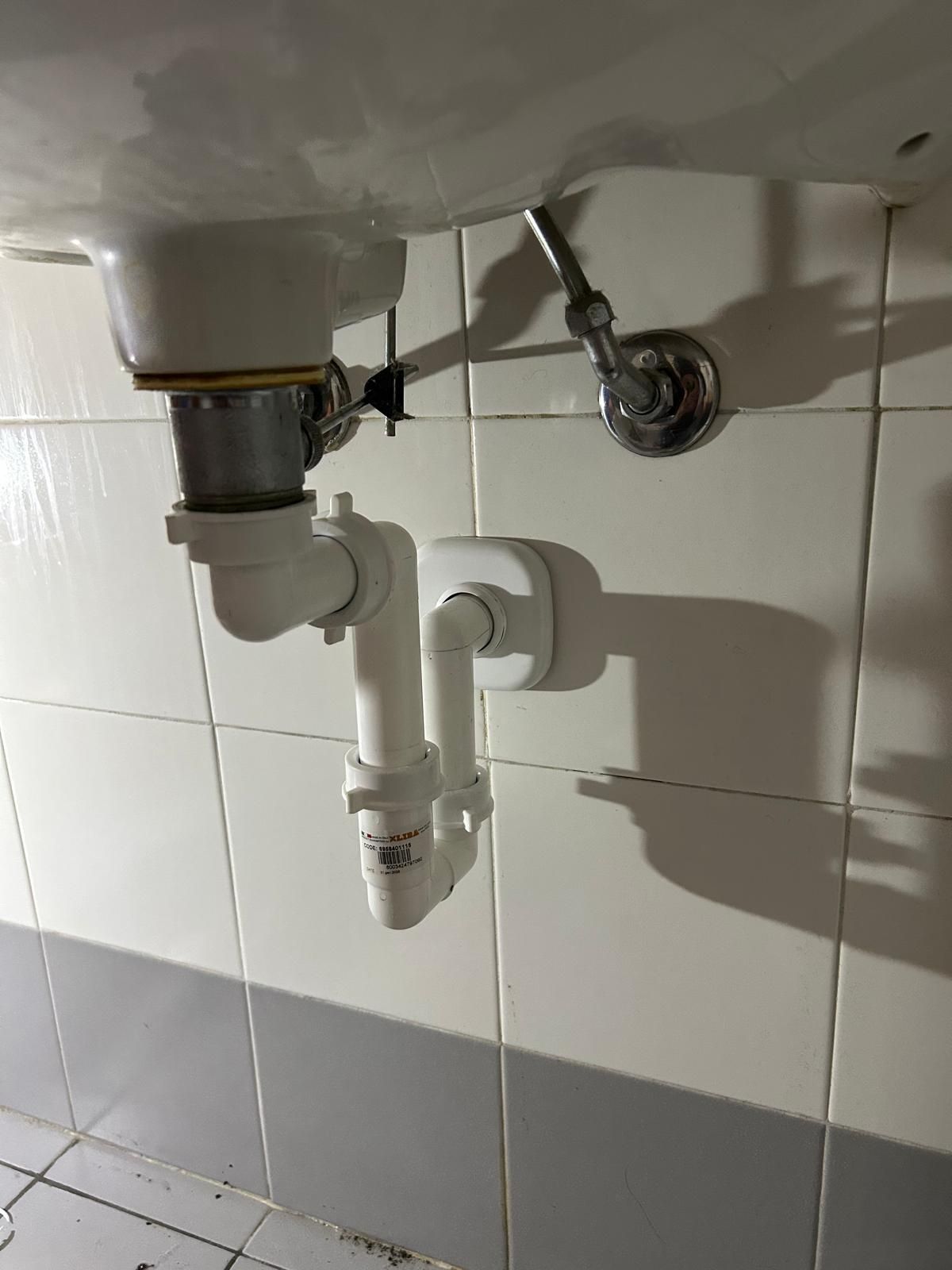 Lavandino bianco del bagno con impianto idraulico visibile contro la parete piastrellata.