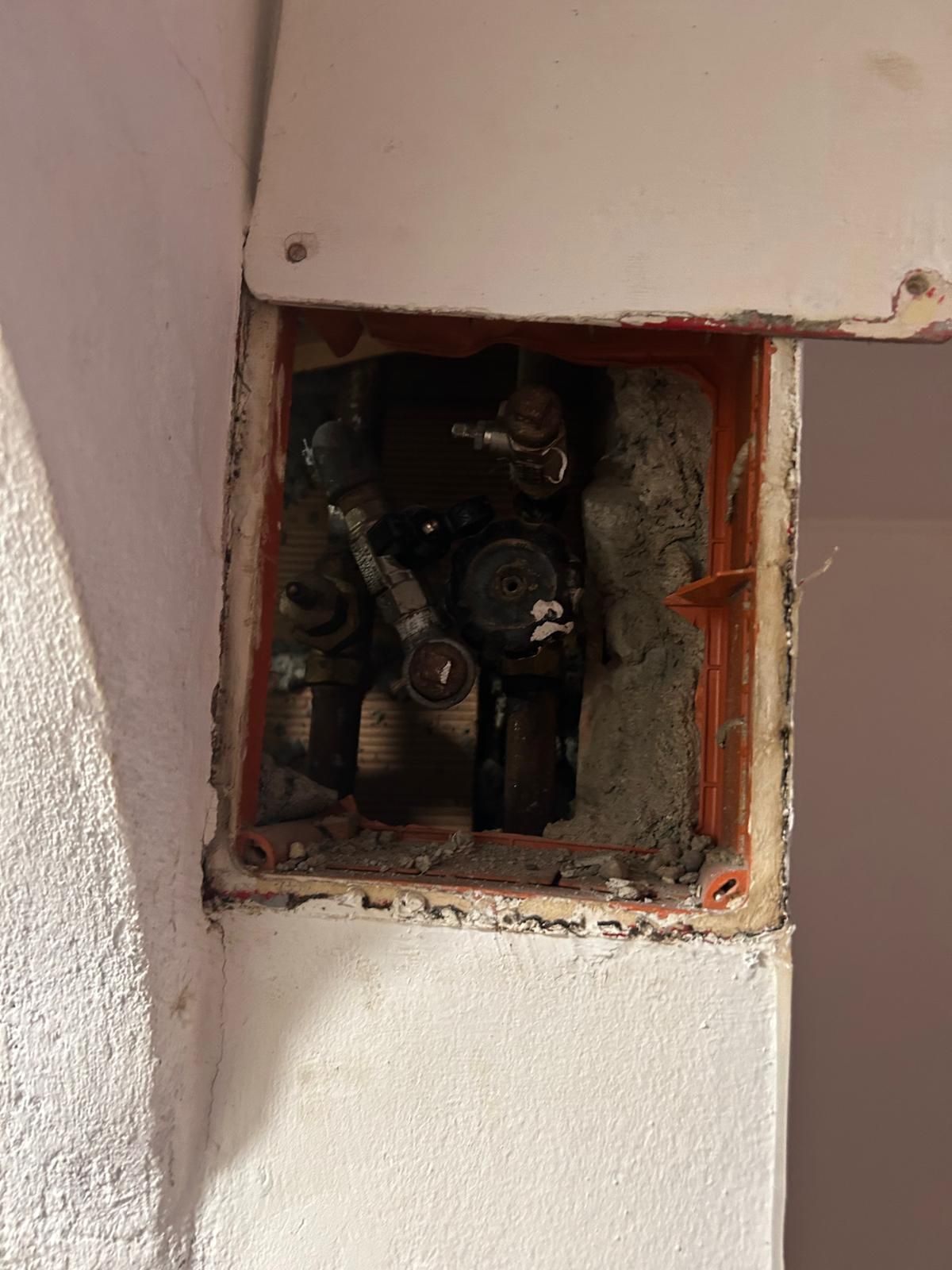 Scatola di derivazione elettrica aperta in un muro. Cemento con fili e connessioni visibili.