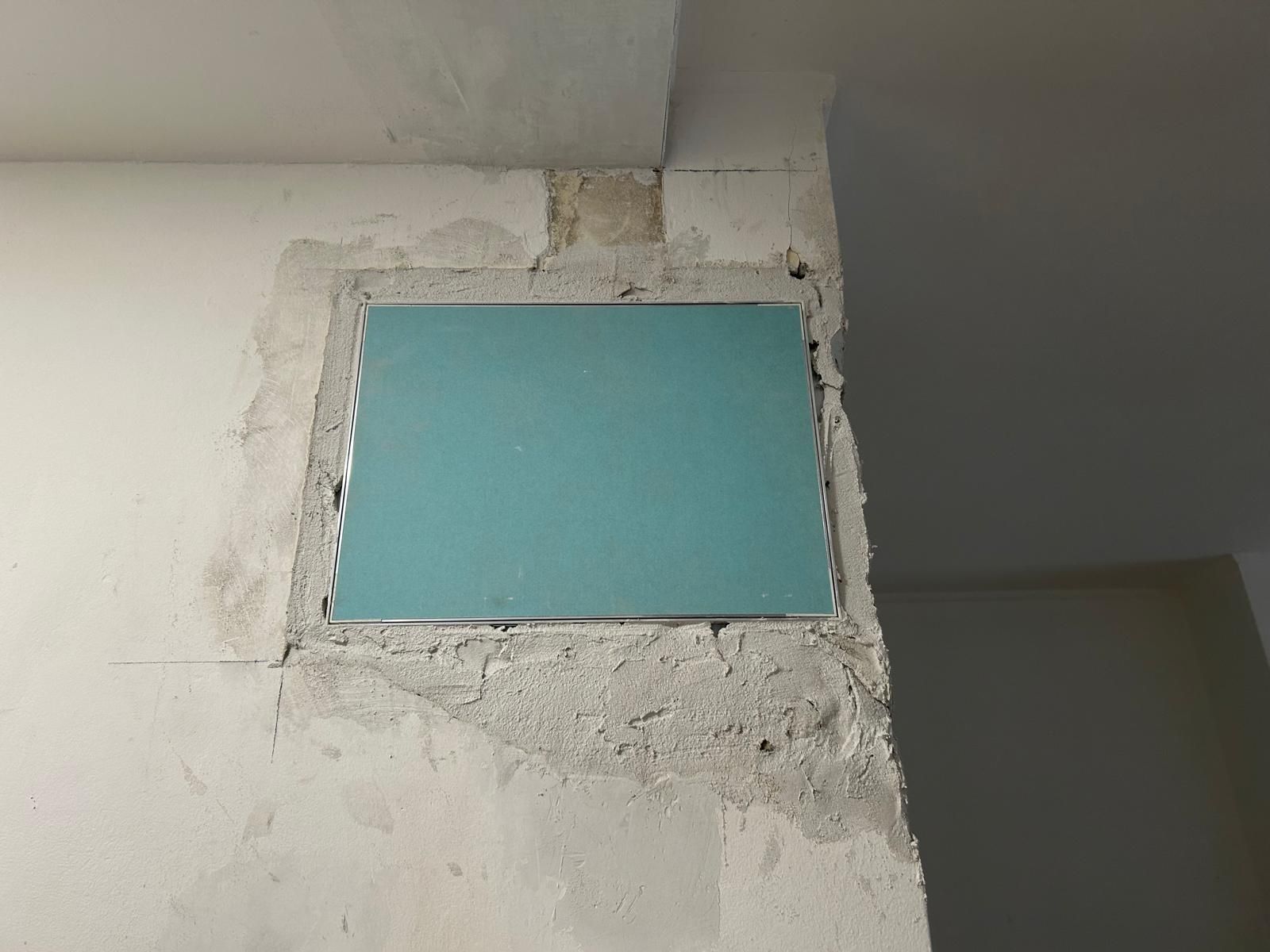 Una toppa di cartongesso blu su un muro danneggiato. Il bordo della toppa è in cemento grigio, incastonato in un angolo bianco.