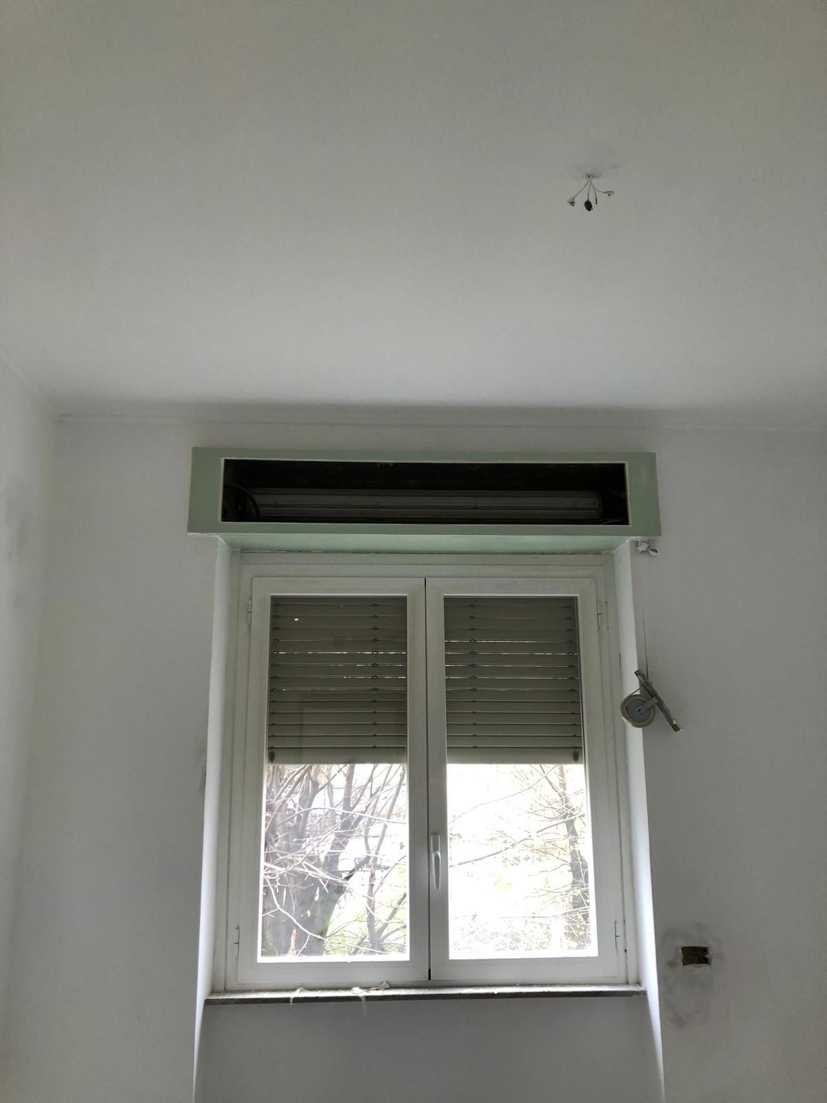 Finestra con persiane chiuse e lampada sopra, in una stanza bianca.