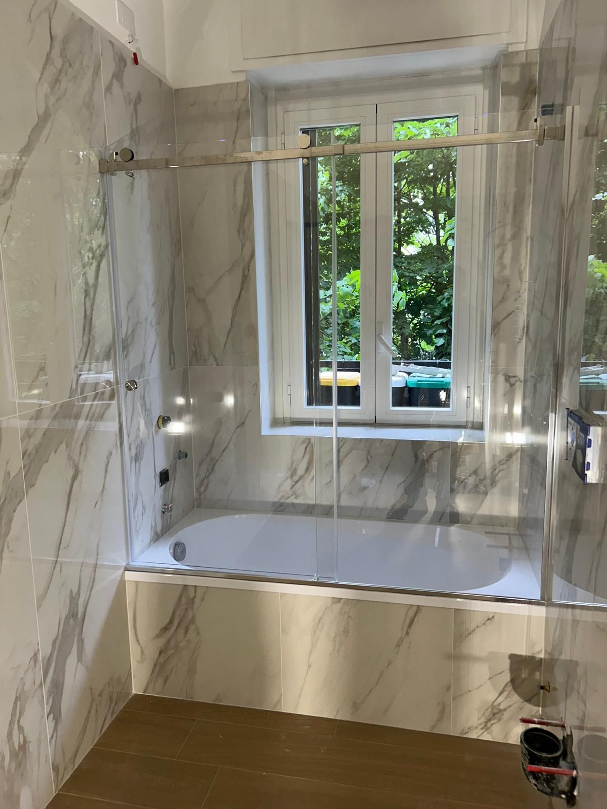 Bagno con piastrelle in marmo bianco e grigio, vasca da bagno e porta doccia in vetro.