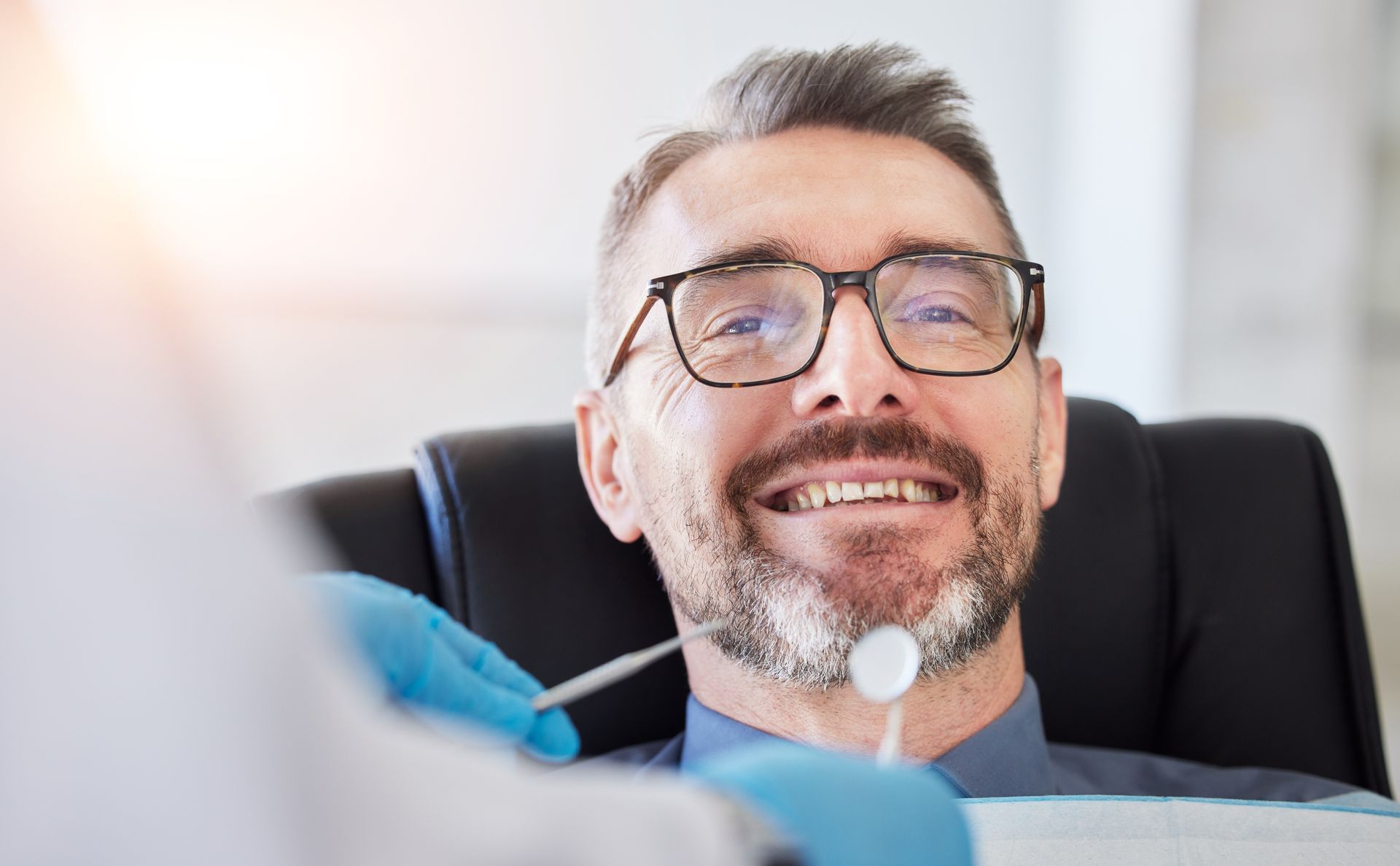 Man in dental chair smiling, dentist holding tools.